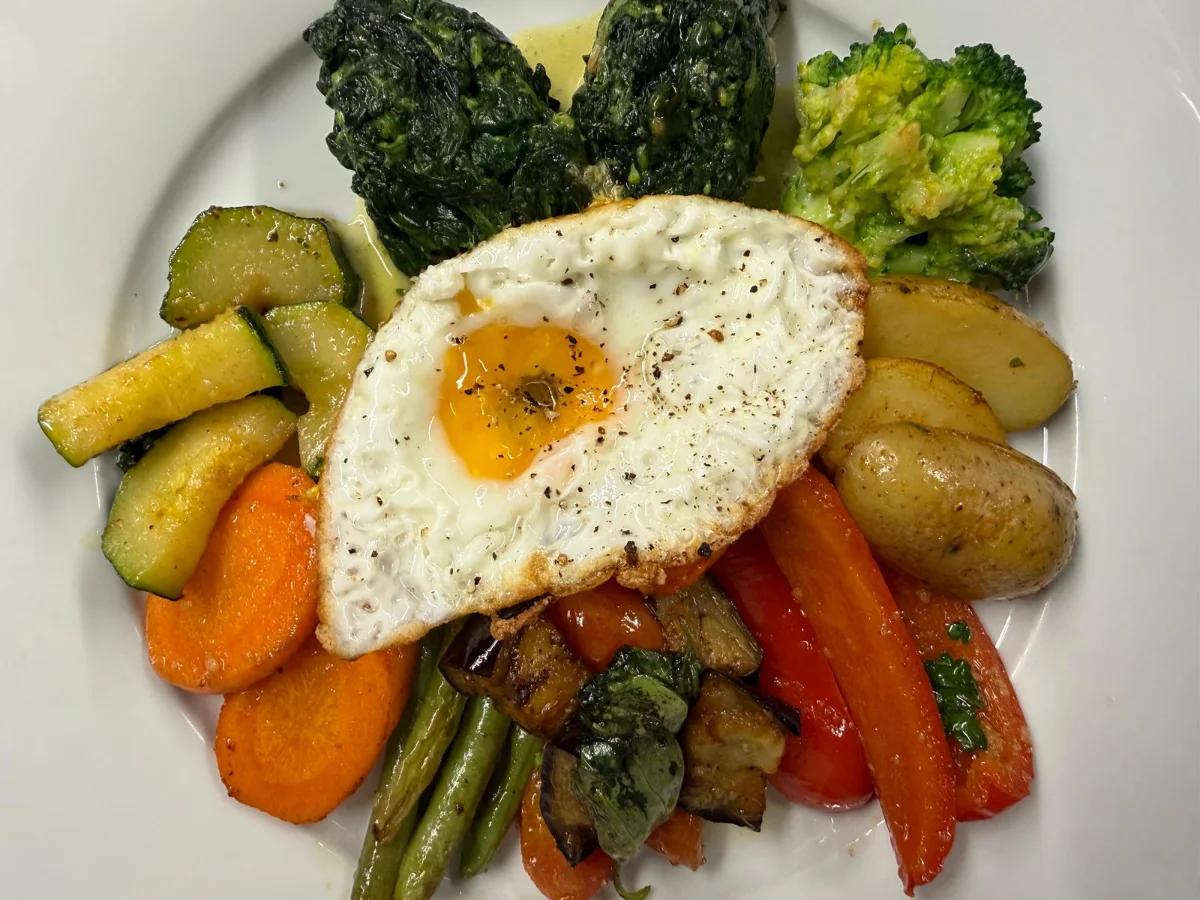 Ein Teller mit gebratenem Fisch, goldenen Kartoffeln und einer frischen Orangenscheibe.