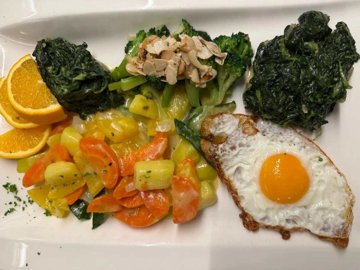 Ein Teller mit gebratenem Fisch, goldenen Kartoffeln und einer frischen Orangenscheibe.