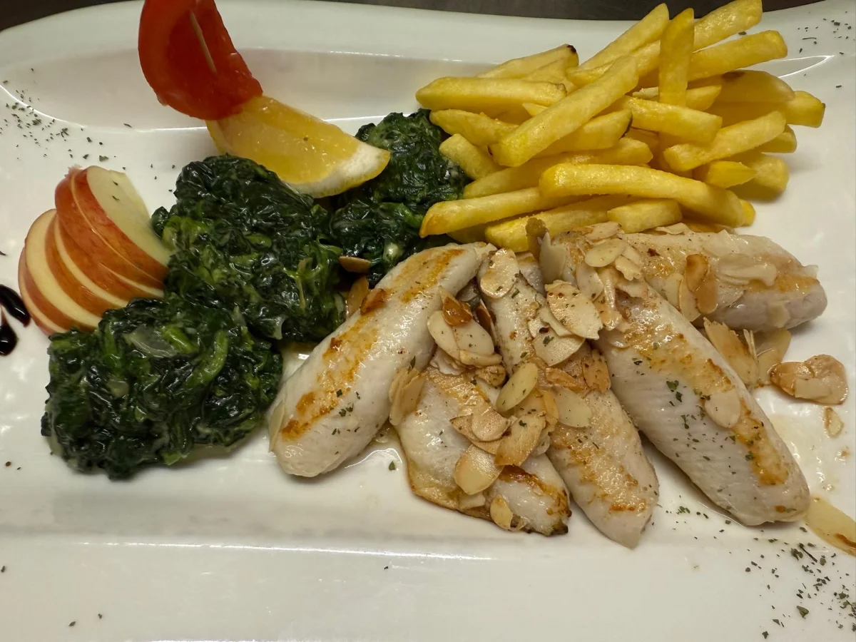 Ein Teller mit gebratenem Fisch, goldenen Kartoffeln und einer frischen Orangenscheibe.