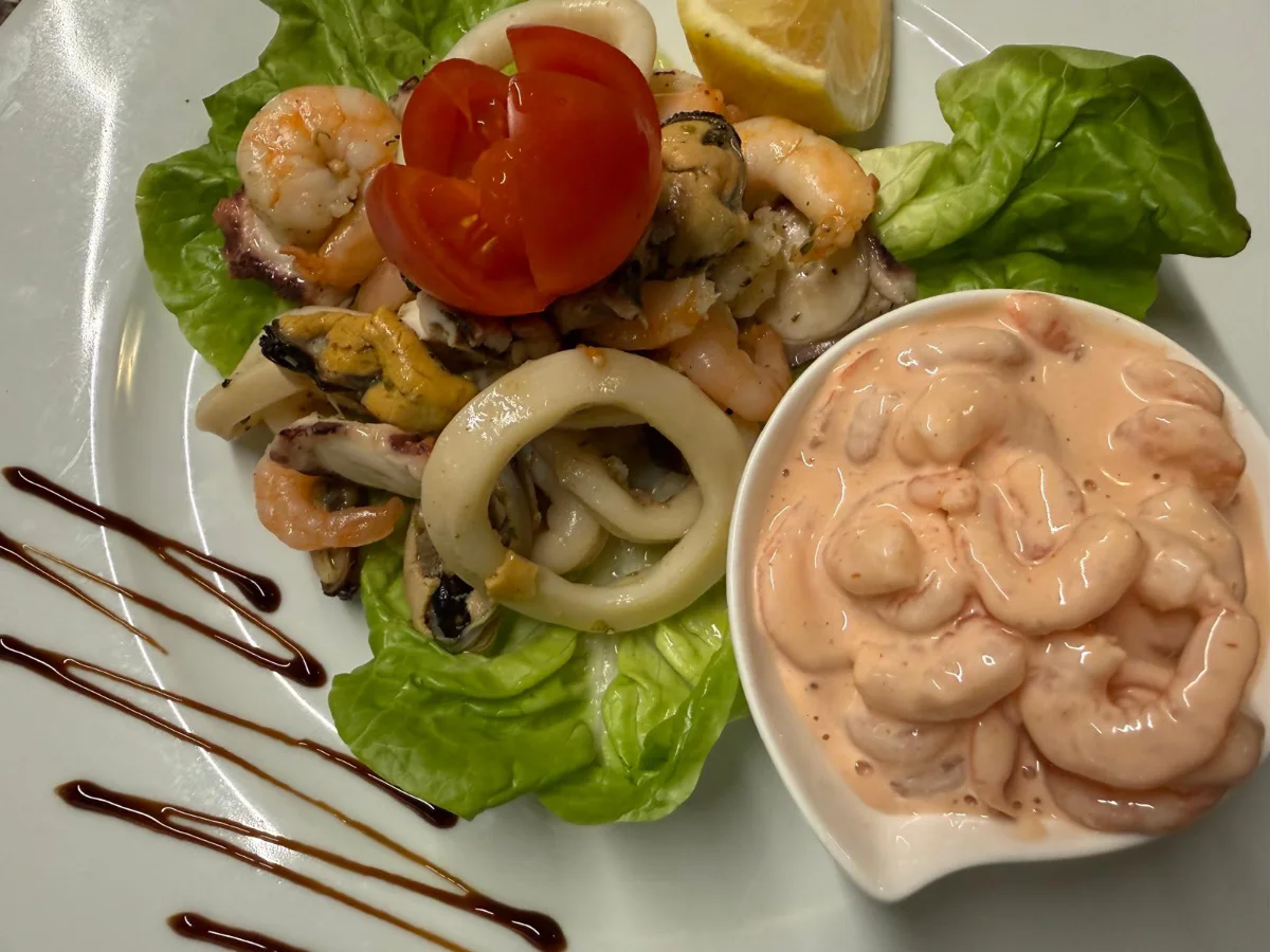 Ein Teller mit gebratenem Fisch, goldenen Kartoffeln und einer frischen Orangenscheibe.
