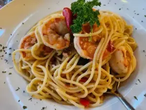 Eine Portion Spaghetti mit saftigen Garnelen und frischem Gemüse auf einem weißen Teller.