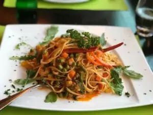Ein Teller Spaghetti mit buntem Gemüse und frischen Blättern.
